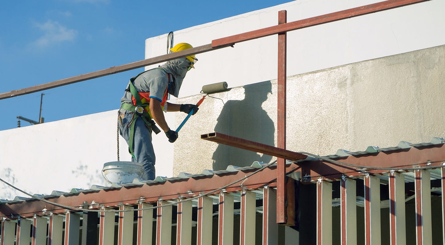A man using a roller to paint a wall in a white color.